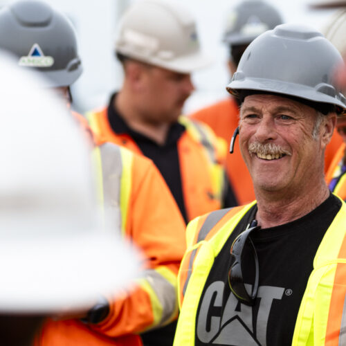 OSWCA, close up, employees all around, focus on smiling employee, gray hard hat, cat shirt, yellow safety vest, 24053_BUILDWITT_0135
