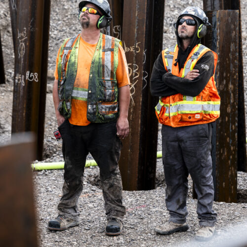 OSWCA, two employees looking up from trench, beams behind them, ear protection, 24053_BUILDWITT_1676