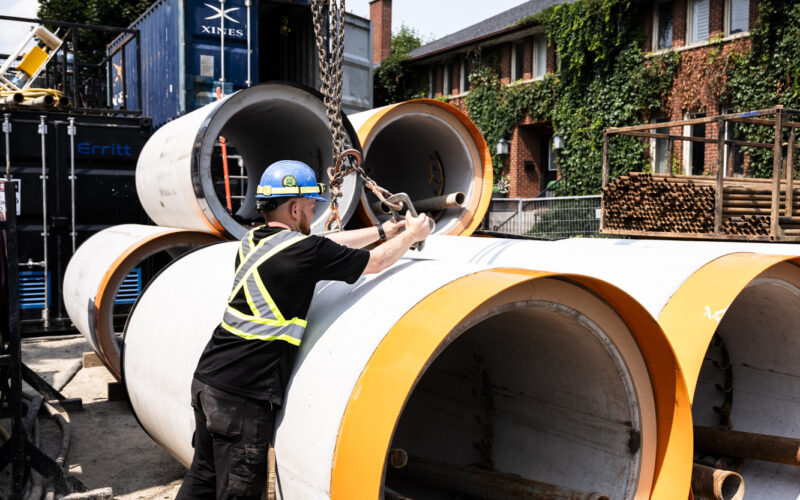 OSWCA, employee, blue hard hat, black clothing, hooking up chain to pipe, vertical, 24067_BUILDWITT_1229