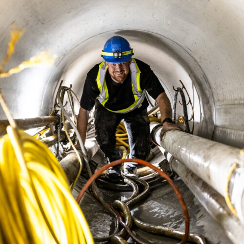 OSWCA, employee inside tunnel, blue hard hat, smiling, yellow rope in left foreground,24067_BUILDWITT_1469