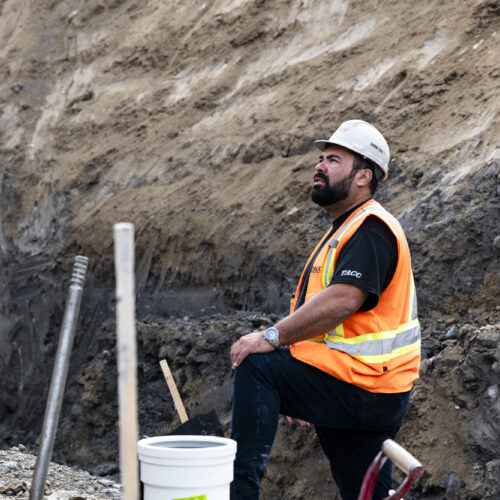 OSWCA, employee, white hard hat, orange safety vest, leg elevated, hand on knee, looking up, 24067_BUILDWITT_1963